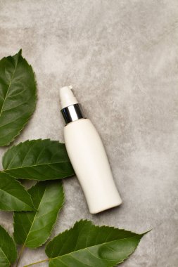 Gri mermer tezgahta beyaz plastik bir şişe ve yeşil yapraklar.