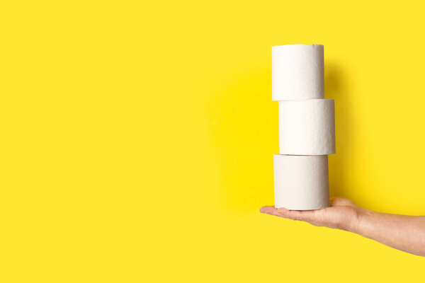 Man hand holding three toilet paper rolls on a yellow background with copy space