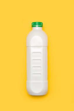 Sarı arka planı yeşil kapaklı beyaz plastik bir şişe.