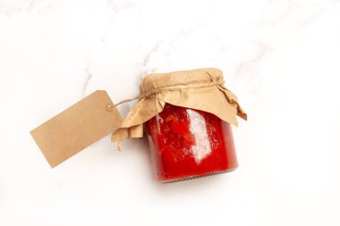 Beyaz arka planda domates sosu dolu boş bir karton etiketle dolu cam bir kavanoz.