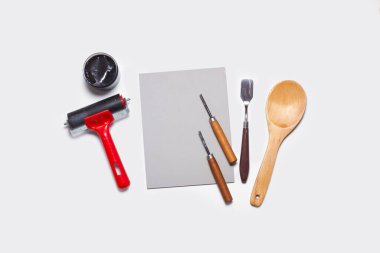 Bir kat muşamba, siyah mürekkep, bir ekran baskı silindiri, spatula, oyuk ve beyaz arka planda bir tahta kaşık.