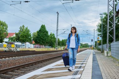 Bavullu bir kadın tren istasyonunun açık platformunda yürüyor. Ulaşım, bagaj, seyahat, tatil, turizm, insan kavramı