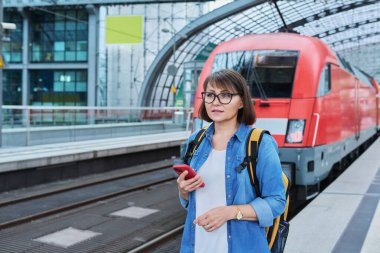 Modern tren istasyonunda şehir demiryolu taşımacılığı yapan kadın yolcu. Akıllı telefonu olan bir kadın, elektrikli tren tarifeli bir web sayfası, online bilet servisi, mobil uygulama üzerinden seyahat için ödeme