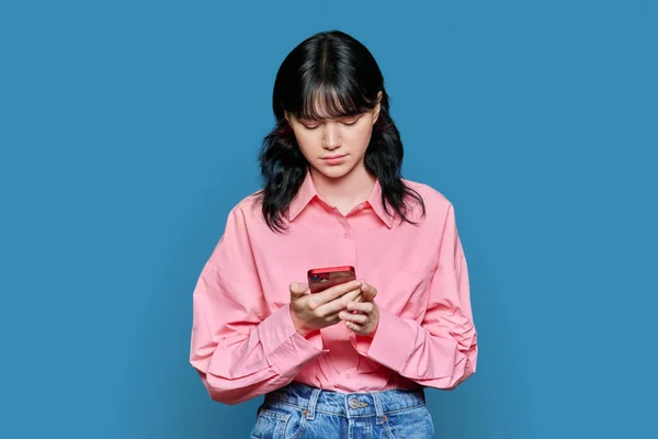 悲伤的年轻女性凝视着智能手机屏幕 蓝色背景 少女读严重的坏消息 — 图库照片