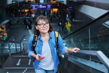 Orta yaşlı bir kadın modern şehir istasyonunun merdivenlerinde. Sırt çantası ve akıllı telefonu olan olgun bir kadın.