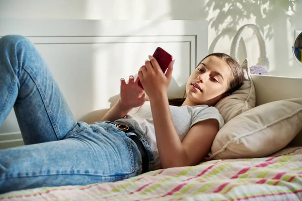 침대에 점심을 소녀가 대화를 스마트폰을 사용하고 소녀가 침실에서 전화로 문자를 — 스톡 사진