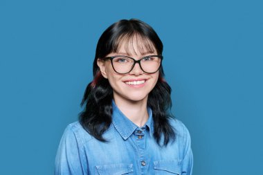 Mavi arka planda kameraya bakan mutlu gülümseyen genç bayan öğrencinin portresi. Çekici kız poz veriyor, dişlek gülümsemesiyle. Eğitim, üniversite, üniversite, gençlik kavramı