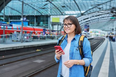 Modern tren istasyonunda şehir demiryolu taşımacılığı yapan kadın yolcu. Akıllı telefonu olan bir kadın, elektrikli tren tarifeli bir web sayfası, online bilet servisi, mobil uygulama üzerinden seyahat için ödeme