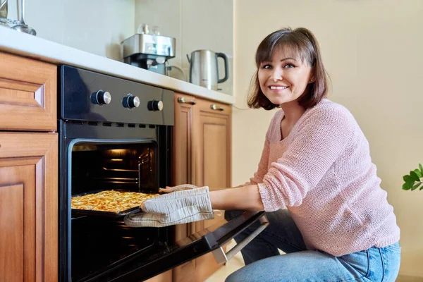 Middle-aged woman with cooked meat taking a baking sheet out of the oven. Home cooking, cooking at home, traditional festive meat dishes concept