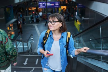Orta yaşlı bir kadın modern şehir istasyonunun merdivenlerinde. Sırt çantası ve akıllı telefonu olan olgun bir kadın.