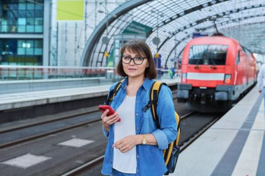 Şehir istasyonunda demiryolu için elektrikli taşımacılık bekleyen bir kadın var. Online bilet ödemesi almak için bankacılık uygulaması kullanan akıllı telefon sahibi bir kadın, çevrimiçi zaman çizelgesi ve rota servisi, teknoloji