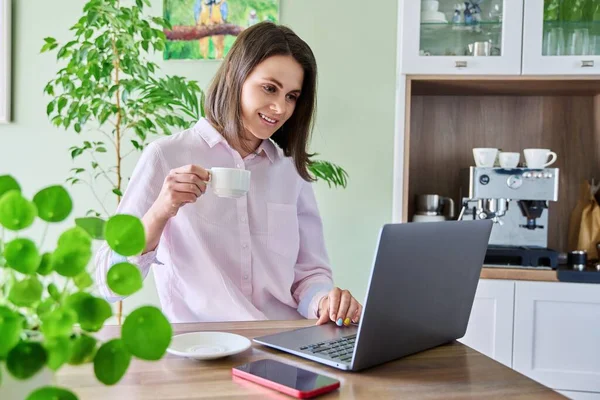 若い女性はノートパソコンを使って家で働いてコーヒーを飲んでいる ライフスタイル フリーランス テクノロジー レジャーの人々の概念 — ストック写真