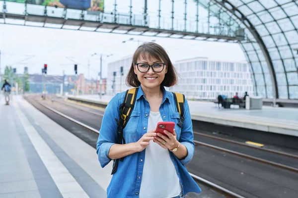 Mature Happy Woman Smartphone Backpack Looking Camera Modern Train Station — Stock Photo, Image