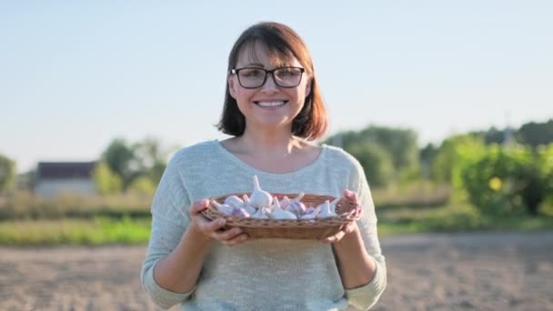 中年妇女的大蒜收获在柳条箱 室外蔬菜园 微笑的女性看着相机夏天秋天的自然收获 农业耕作 自然生态食品 健康饮食 — 图库视频影像