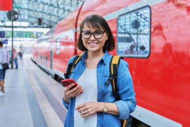 Modern tren istasyonunda şehir demiryolu taşımacılığı yapan kadın yolcu. Akıllı telefonu olan bir kadın, elektrikli tren tarifeli bir web sayfası, online bilet servisi, mobil uygulama üzerinden seyahat için ödeme