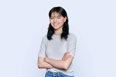 Portrait of confident positive young teenage female student with arms crossed over white studio background. Beautiful brunette woman in white clothes looking at camera with toothy smile clipart