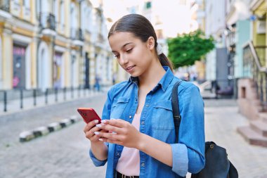 Akıllı telefon kullanan güzel bir genç kız, şehir geçmişi. Şehir caddesinde telefon ekranına bakan çekici, genç bir bayan. Teknoloji, eğlence, eğlence, yaşam tarzı, gençlik kavramı