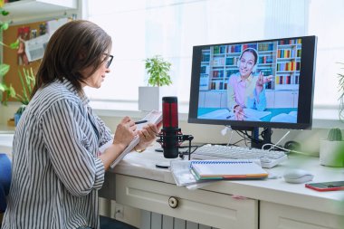 Mature woman talking online with teenage girl using video call on computer, home interior. Virtual meeting, therapy session with psychologist. Chat conference technology psychology education learning