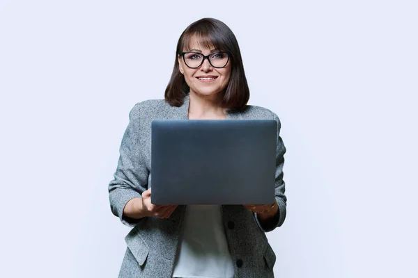 Middle age business woman with laptop looking at camera on white studio background. Positive successful mature female using laptop for business, service. Entrepreneurship finance employment study