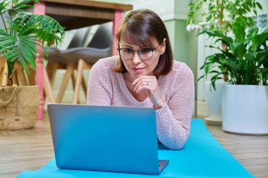 Orta yaşlı bir kadın evdeki paspasın üzerinde dizüstü bilgisayarla yatıyor. Yaşam tarzı, boş zaman, insanların konsepti