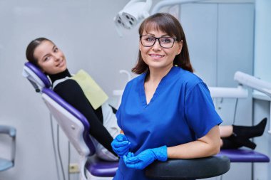 Dişçi koltuğunda oturan genç kız hastayla kameraya bakan gülümseyen kadın dişçinin portresi. Dişçi muayenesine git. Diş sağlığı diş sağlığı diş sağlığı konsepti