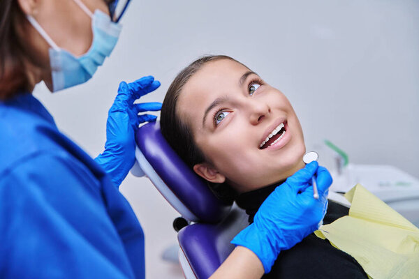 Young teenage female at dental examination treatment checkup in clinic. Teen girl sitting in chair doctor dentist with tools examining patient teeth. Adolescence hygiene dentistry dental health care