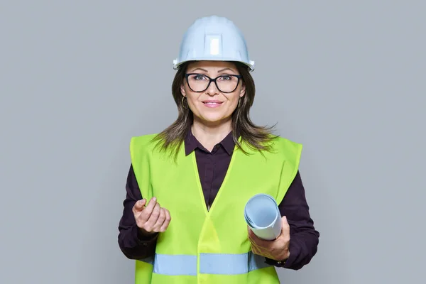 建筑图纸上的女工程师设计师穿着头盔保护背心 在灰色工作室的背景下看着相机 建筑工程概念 — 图库照片