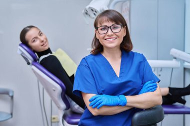 Dişçi koltuğunda oturan genç kız hastayla kameraya bakan gülümseyen kadın dişçinin portresi. Dişçi muayenesine git. Diş sağlığı diş sağlığı diş sağlığı konsepti