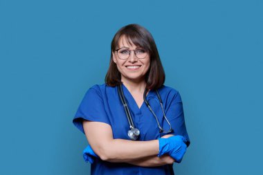 Steteskoplu hemşire doktor kadının portresi mavi renkli stüdyo arkaplanındaki kameraya bakıyor. Mavi üniformalı, dost canlısı bir sağlık görevlisi. İlaç, personel, sağlık hizmetleri kavramı