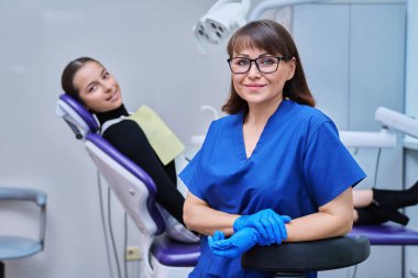 Dişçi koltuğunda oturan genç kız hastayla kameraya bakan gülümseyen kadın dişçinin portresi. Dişçi muayenesine git. Diş sağlığı diş sağlığı diş sağlığı konsepti
