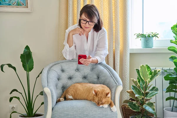 Middelbare Vrouw Met Smartphone Huis Met Slapende Kat Fauteuil Kamerplanten — Stockfoto