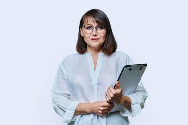 Beyaz arka plandaki kameraya bakan orta yaşlı, kendine güvenen bir iş kadını. Olgun gülümseyen bayan öğretmen ajan müfettiş psikolog evraklarla poz veriyor.