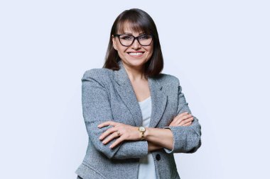 Beyaz stüdyo geçmişinde kollarını kavuşturmuş orta yaşlı bir iş kadını. Kendine güvenen, dişlek gülüşlü, kamera reklamlarına bakan bir kadın. İş yönetimi başarı personeli