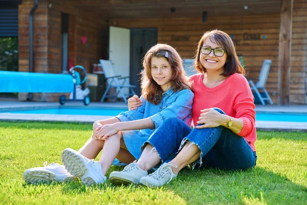 Portrait of happy mom and teenage daughter looking at camera. Smiling hugging mother and girl together in backyard near outdoor pool. Family, parent and child teenager, mothers day, lifestyle concept