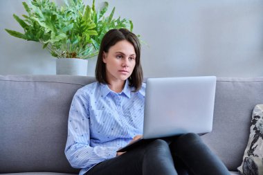 Kanepede dizüstü bilgisayar kullanarak çalışan genç bir iş kadını. Serbest çalışma, uzaktan çalışma, çevrimiçi iş, teknoloji, satış, e-öğrenme, e-eğitim kavramı