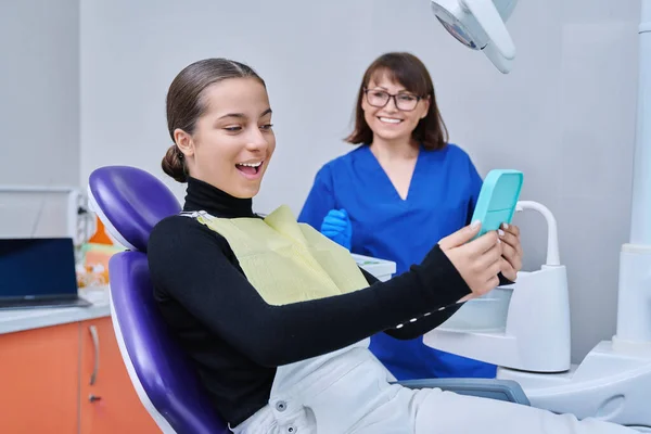 Szczęśliwa Młoda Nastoletnia Kobieta Lustrem Siedząca Fotelu Dentystycznym Uśmiechnięta Patrząc — Zdjęcie stockowe