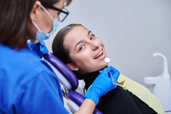 Young teenage female at dental examination treatment checkup in clinic. Teen girl sitting in chair doctor dentist with tools examining patient teeth. Adolescence hygiene dentistry dental health care