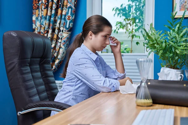 Teenage upset girl crying in front of computer screen. Young unhappy female with napkins in her hands watching reading bad sad movie, news, wiping her tears