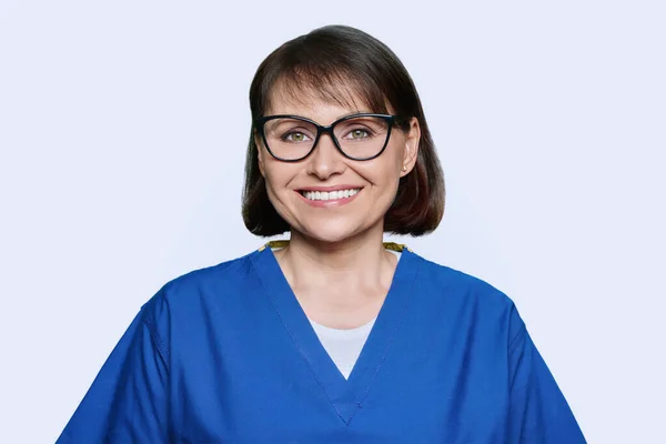 穿着蓝色衣服的中年女护士微笑着 看着摄像机 照片背景是美丽的演播室 医务人员概念 — 图库照片
