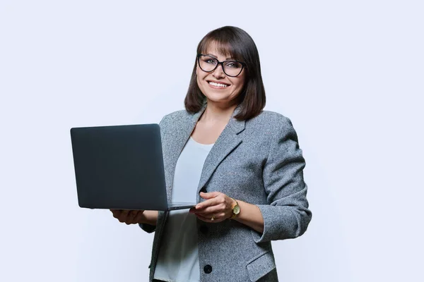 Middle age business woman with laptop looking at camera on white studio background. Positive successful mature female using laptop for business, service. Entrepreneurship finance employment study
