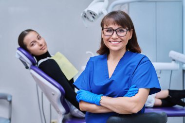 Dişçi koltuğunda oturan genç kız hastayla kameraya bakan gülümseyen kadın dişçinin portresi. Dişçi muayenesine git. Diş sağlığı diş sağlığı diş sağlığı konsepti