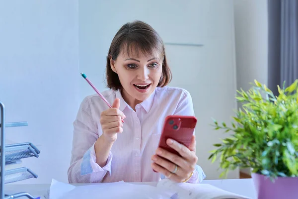 Woman using smart phone for meeting video call sitting at workplace in home office. Technology, business, education, people concept