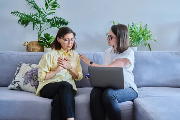 Middle aged woman in individual therapy, female psychologist and patient sitting together on couch in office. Psychology, counseling, psychotherapy, mental health, health care, mature people concept