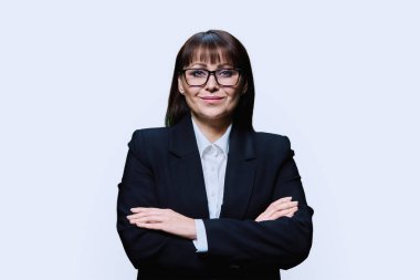 Hafif stüdyo arka planında beyaz takım elbiseli, orta yaşlı, kendine güvenen bir iş kadını. Kollarını kavuşturup kameraya bakan bir iş kadını. Liderlik yönetimi finans bankacısı iş adamı