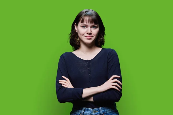 年轻微笑的女性在镜头前的肖像 交叉的臂膀在绿色的工作室背景上 快乐快乐积极的女性18 19岁 生活方式 青年概念 — 图库照片