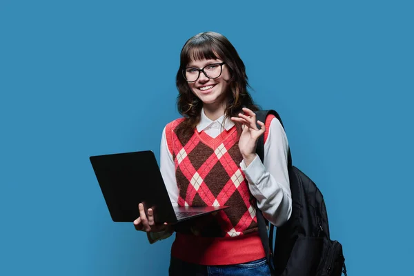 Smiling female student 18, 19 years old looking in camera on blue studio background. Cheerful girl in glasses using internet for study, e-learning, online lessons, college university courses