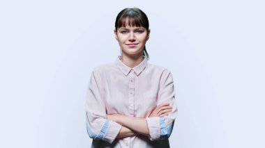 Portrait of young smiling female looking at camera, with crossed arms on white studio background. Happy cheerful positive female 18, 19 years old. Lifestyle, youth concept