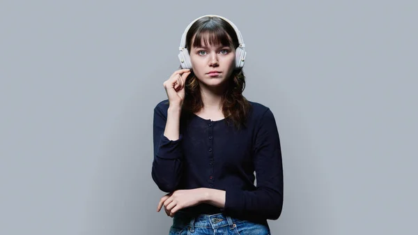 认真沉思的年轻女性 戴着耳机 看着镜头 双手放在灰色工作室背景上 张嘴闭着嘴 — 图库照片