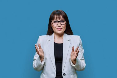Portrait of smiling business confident middle aged woman in white jacket on blue color studio background. Leadership, management, teaching, finance, insurance, banker, businessperson staff concept