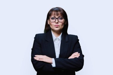 Confident serious middle aged business woman in suit on light studio background. Businesswoman with crossed arms looking at camera. Leadership management teaching finance banker businessperson